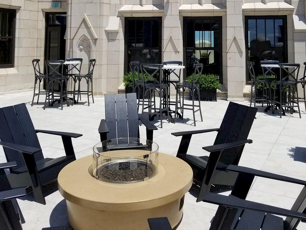 This image shows an outdoor patio with chairs around a fire pit, set against a building with ornate architecture and arched windows.