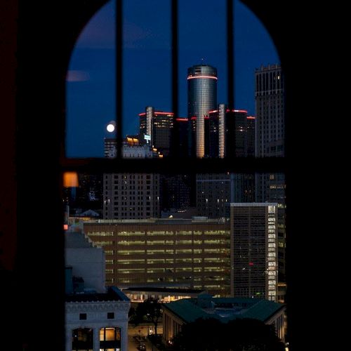 A cityscape viewed through an arched window at night, highlighting illuminated skyscrapers and the bright city lights.